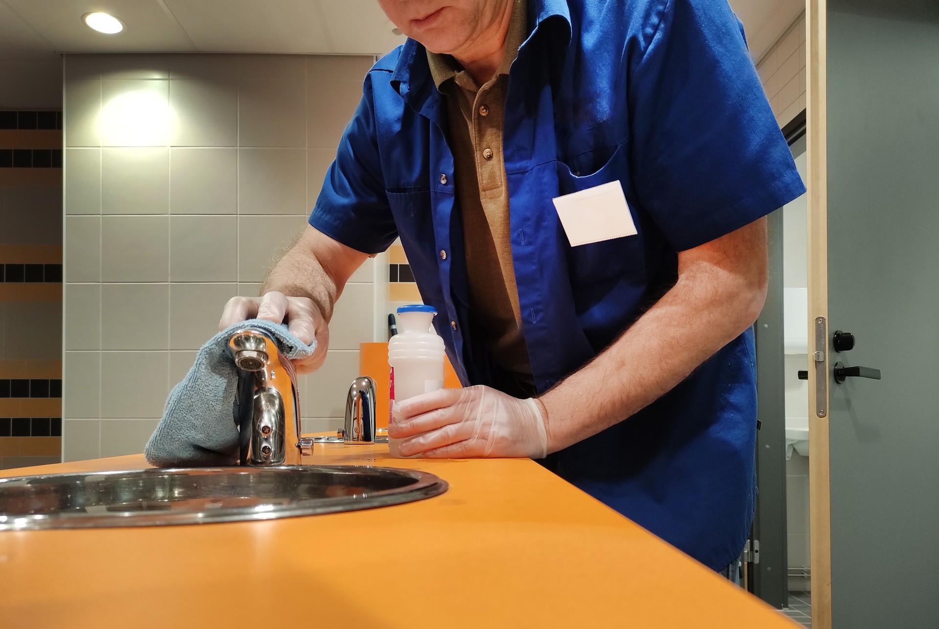 A male cleaner cleans a public toilet, washes the sink and faucet. Cleaning service.
